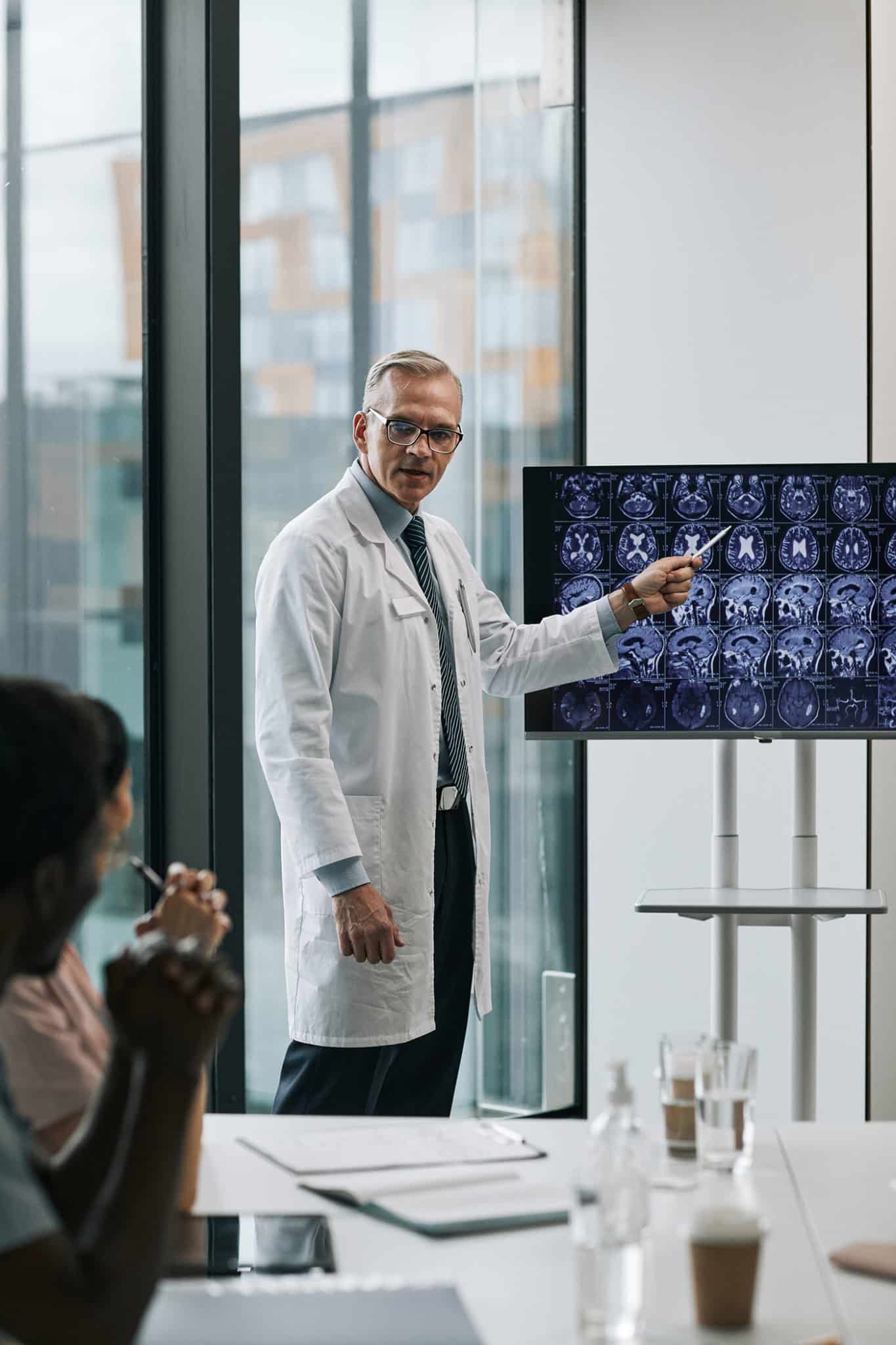 Vertical portrait of mature doctor giving presentation at medical conference and pointing at x-ray images